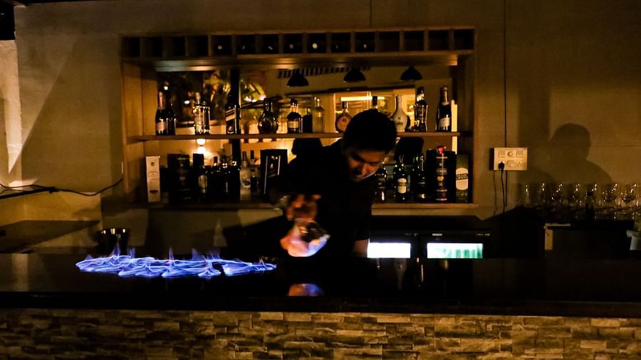 Image of a man behind a counter table with drinks on the shelf behind him at Calux Grand Baga.